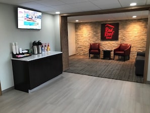A reception area with a counter, a television, a Red Roof Inn sign, and two leather chairs.