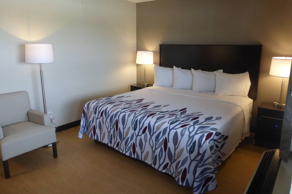 A hotel room with a large bed, two bedside tables with lamps, a chair, and a wall clock.
