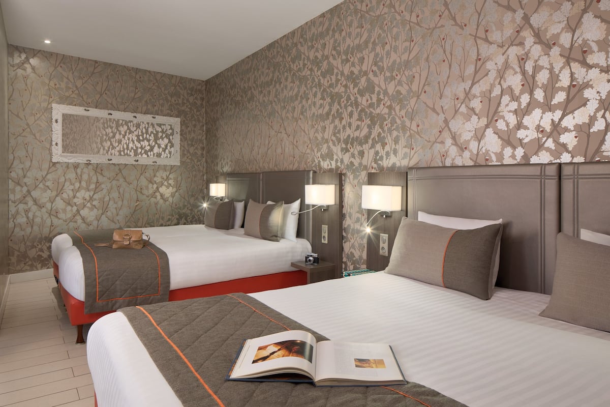 A hotel room with two beds, a large mirror, and a wall with a floral pattern.