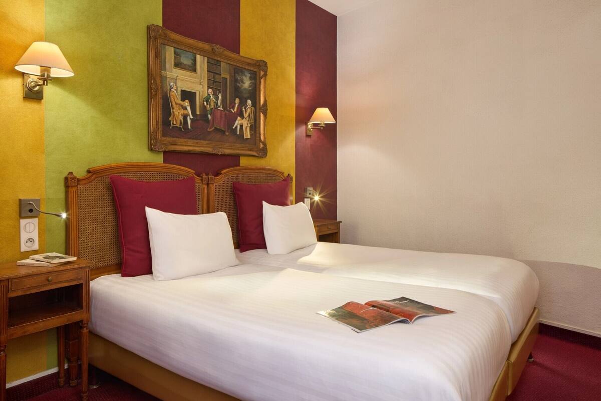 A hotel room with a large bed, two bedside tables, a nightstand, a painting on the wall, and two wall-mounted lamps.
