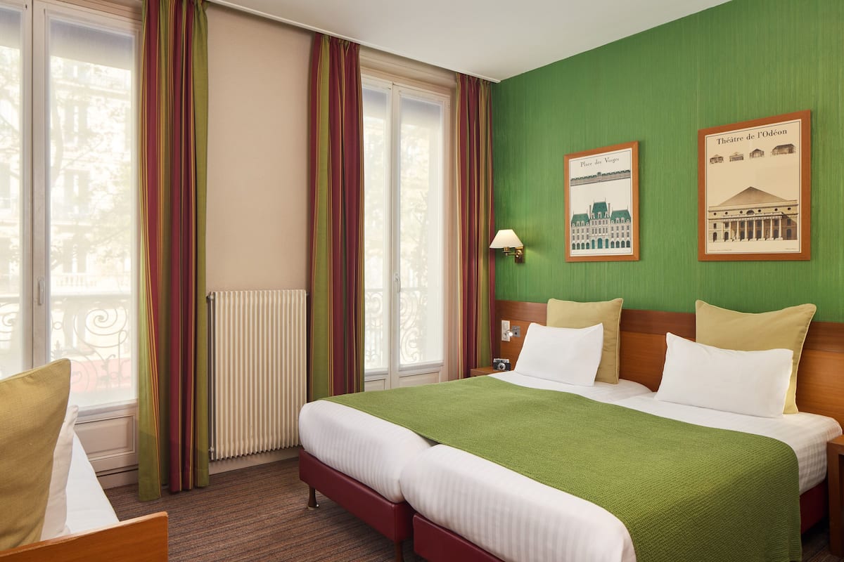 A hotel room with a large bed, a chair, a radiator, curtains, and two framed pictures on the wall.