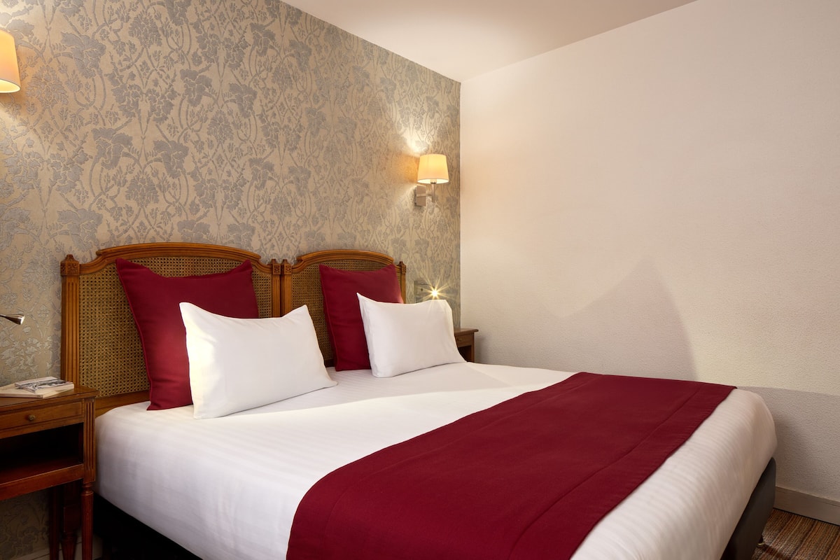 A neatly made bed with a red blanket, two red pillows, and a wooden headboard.