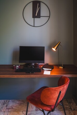 A modern desk with a computer, keyboard, and a vintage camera. A red chair is in front of the desk.