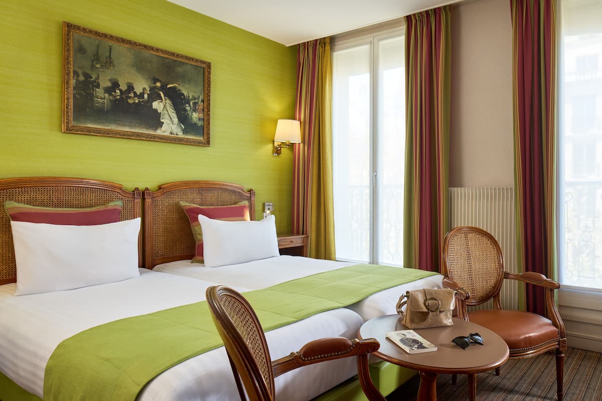 A hotel room with a large bed, two bedside tables, a chair, a small table, and a painting on the wall.