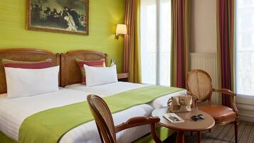 Habitación de hotel con una cama grande, dos mesitas de noche, una silla, una mesita pequeña y un cuadro en la pared.