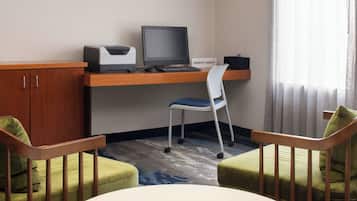 A hotel room with a desk, computer, and two chairs.
