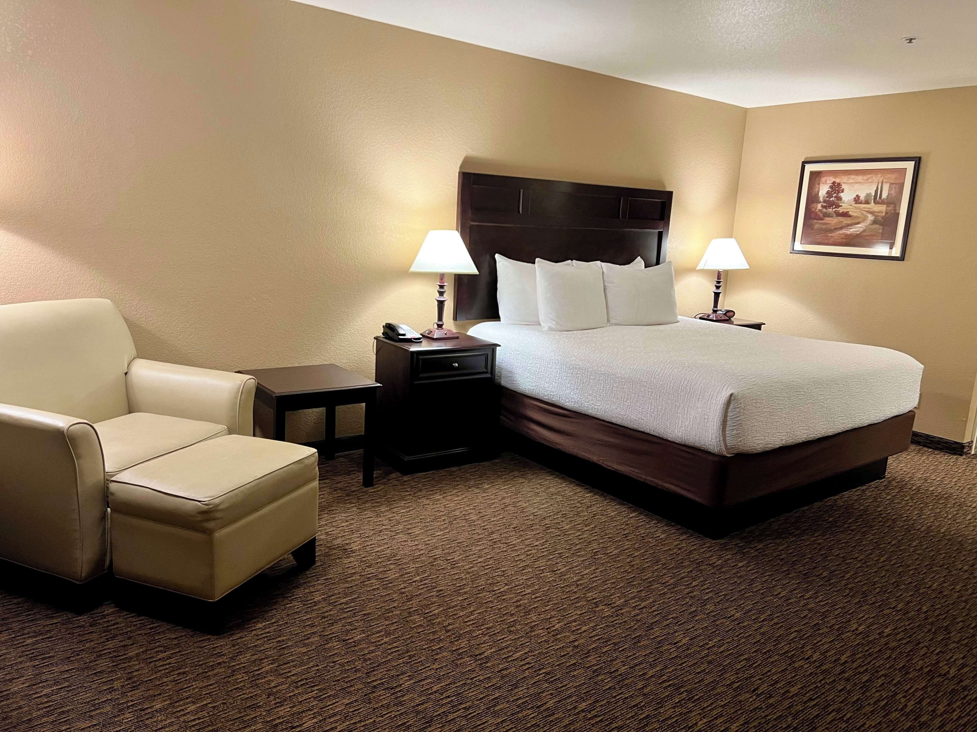 A hotel room with a bed, a chair, a nightstand, and a lamp.
