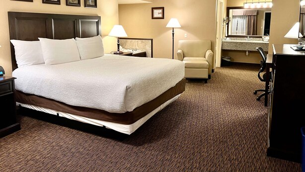 A hotel room with a large bed, a chair, a desk, and a bathroom visible through an open door.