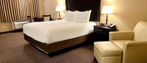 A hotel room with a large bed, two bedside lamps, a chair, and a desk with a phone.
