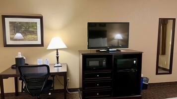 A hotel room with a desk, chair, television, lamp, and a minibar.