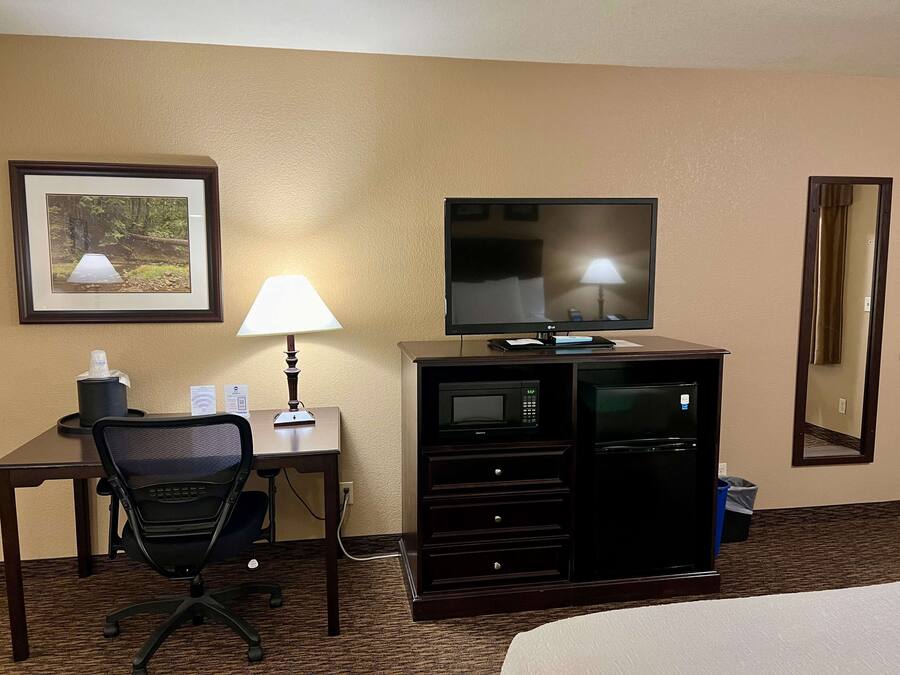 A hotel room with a desk, chair, television, lamp, and a minibar.