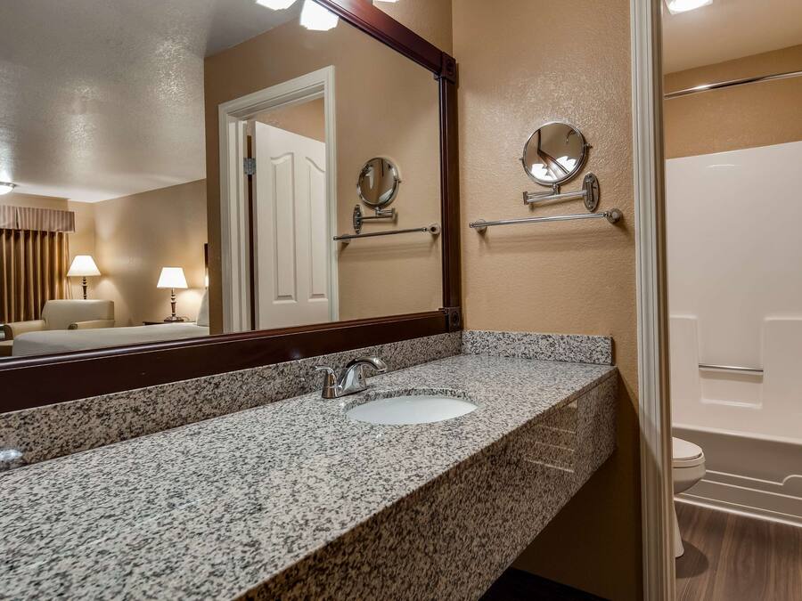 A hotel bathroom with a granite countertop sink, a mirror, a towel rack, and a bathtub.