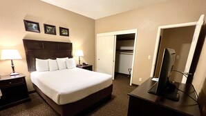 A hotel room with a large bed, two bedside tables with lamps, a desk with a computer, a mirror, and a wardrobe.