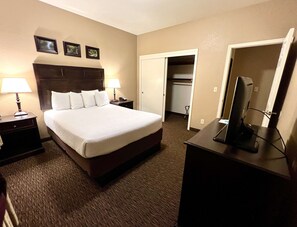 A hotel room with a large bed, two bedside tables with lamps, a desk with a computer, a mirror, and a wardrobe.