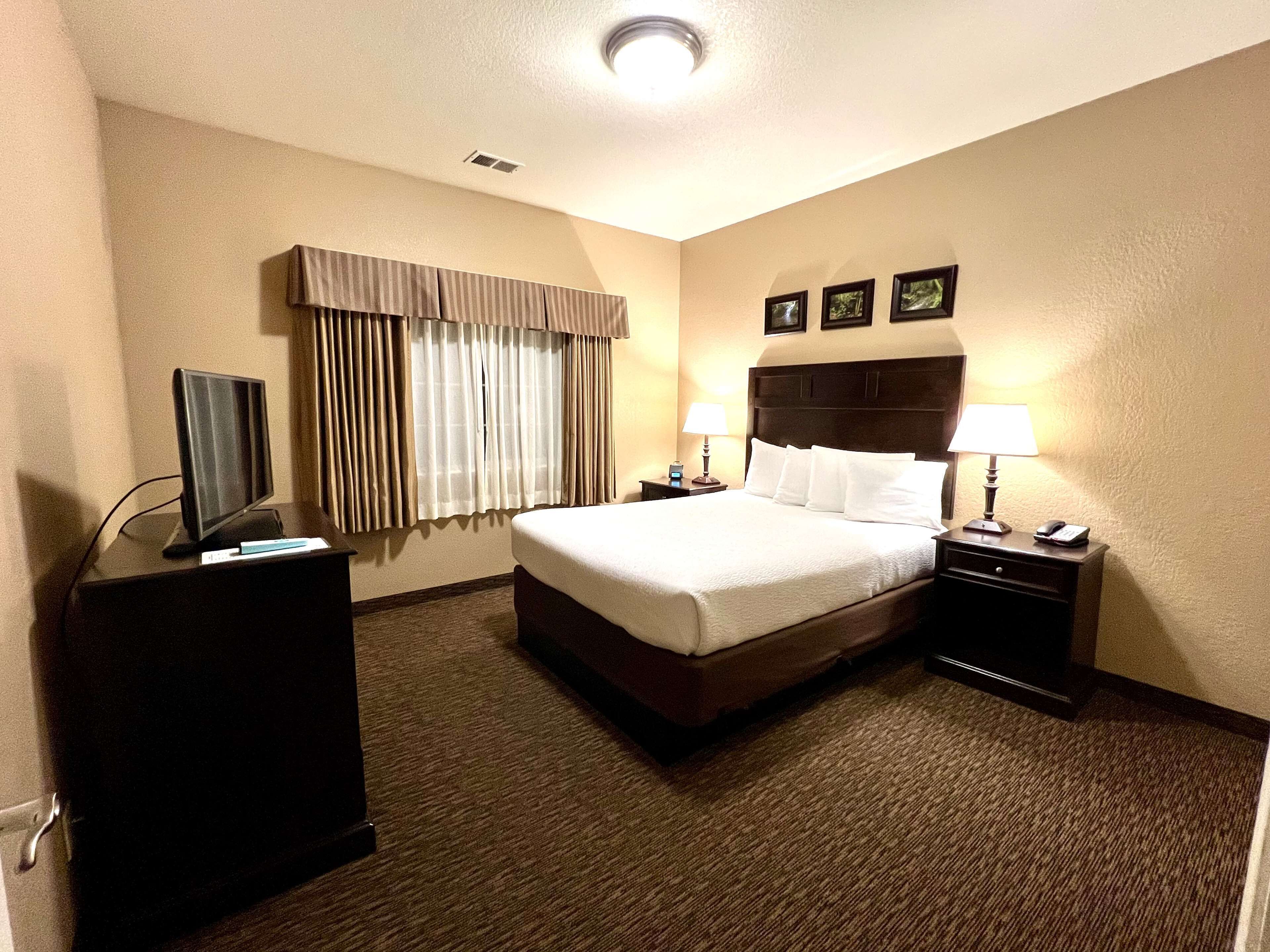 Habitación de hotel con una cama grande, un escritorio con computadora, una lámpara y un televisor.