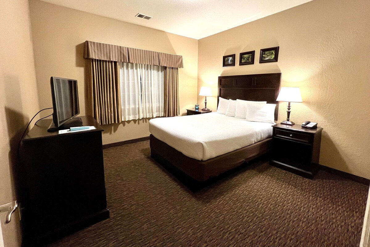 A hotel room with a large bed, a desk with a computer, a lamp, and a TV.