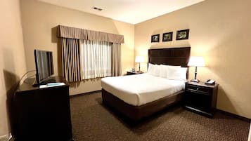 Habitación de hotel con una cama grande, un escritorio con computadora, una lámpara y un televisor.