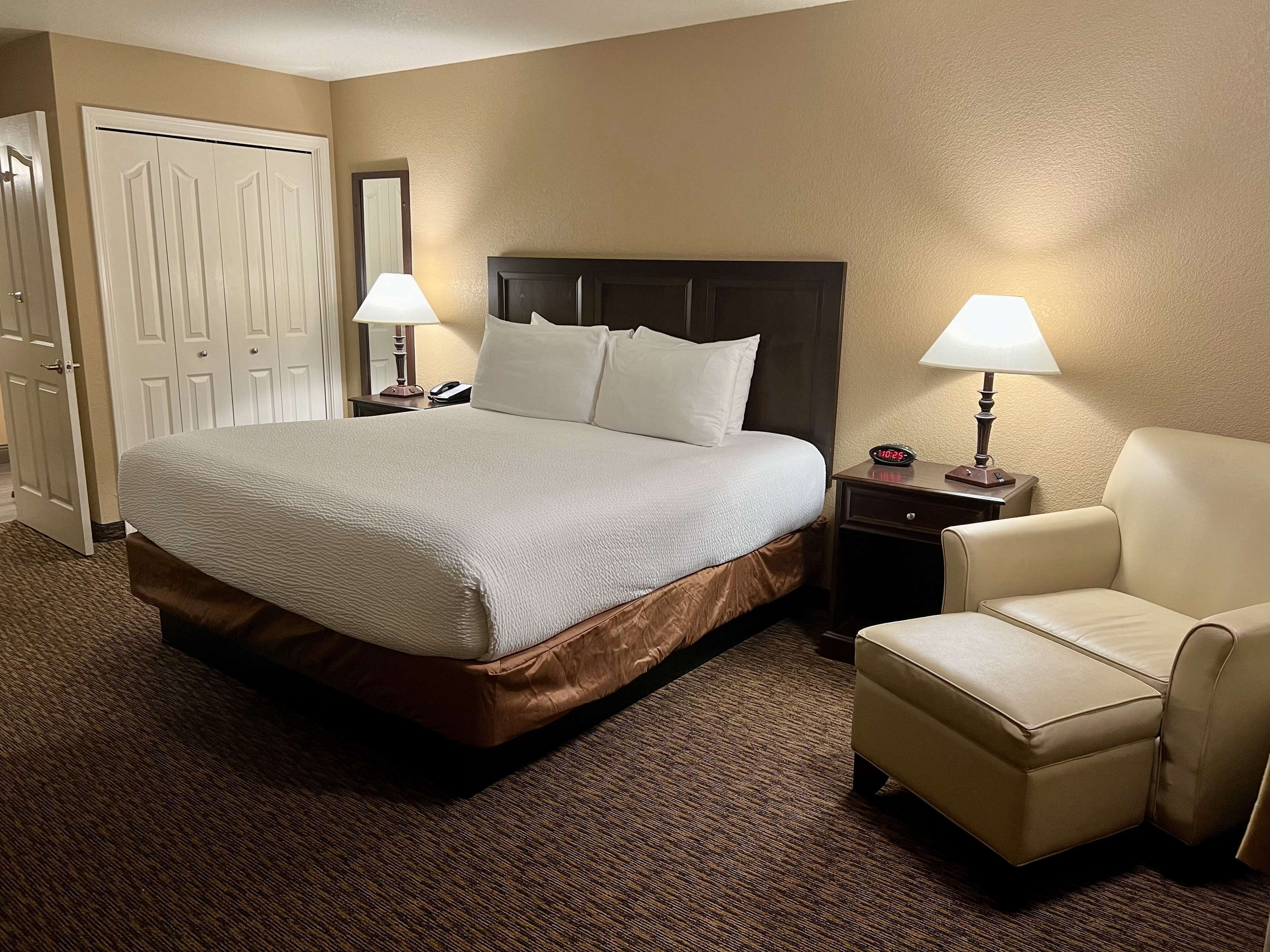 Habitación de hotel con una cama grande, dos mesitas de noche con lámparas, una silla y un armario.