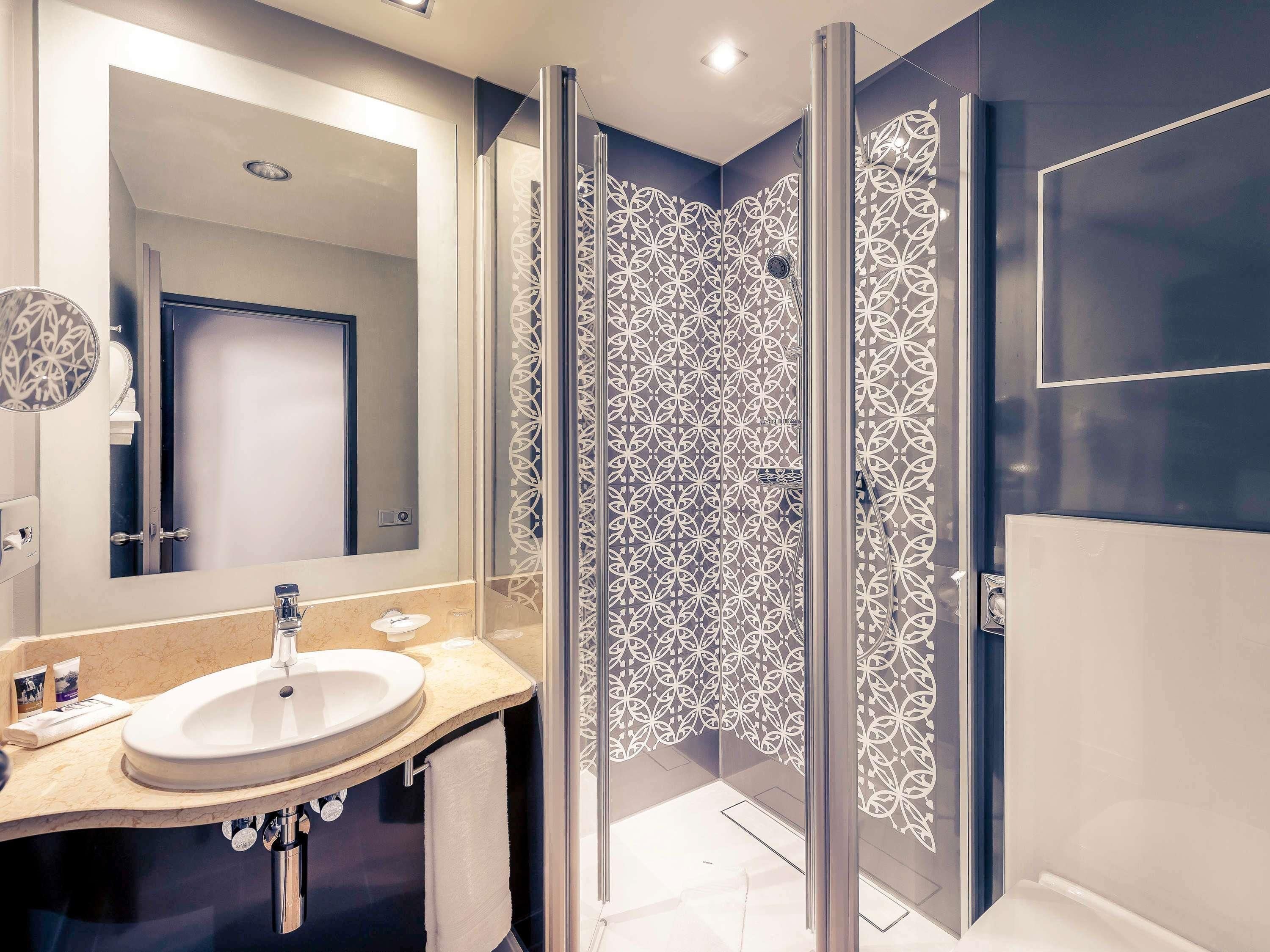 Un baño moderno con un espejo grande, un lavamanos y una ducha con paneles de vidrio decorativos.