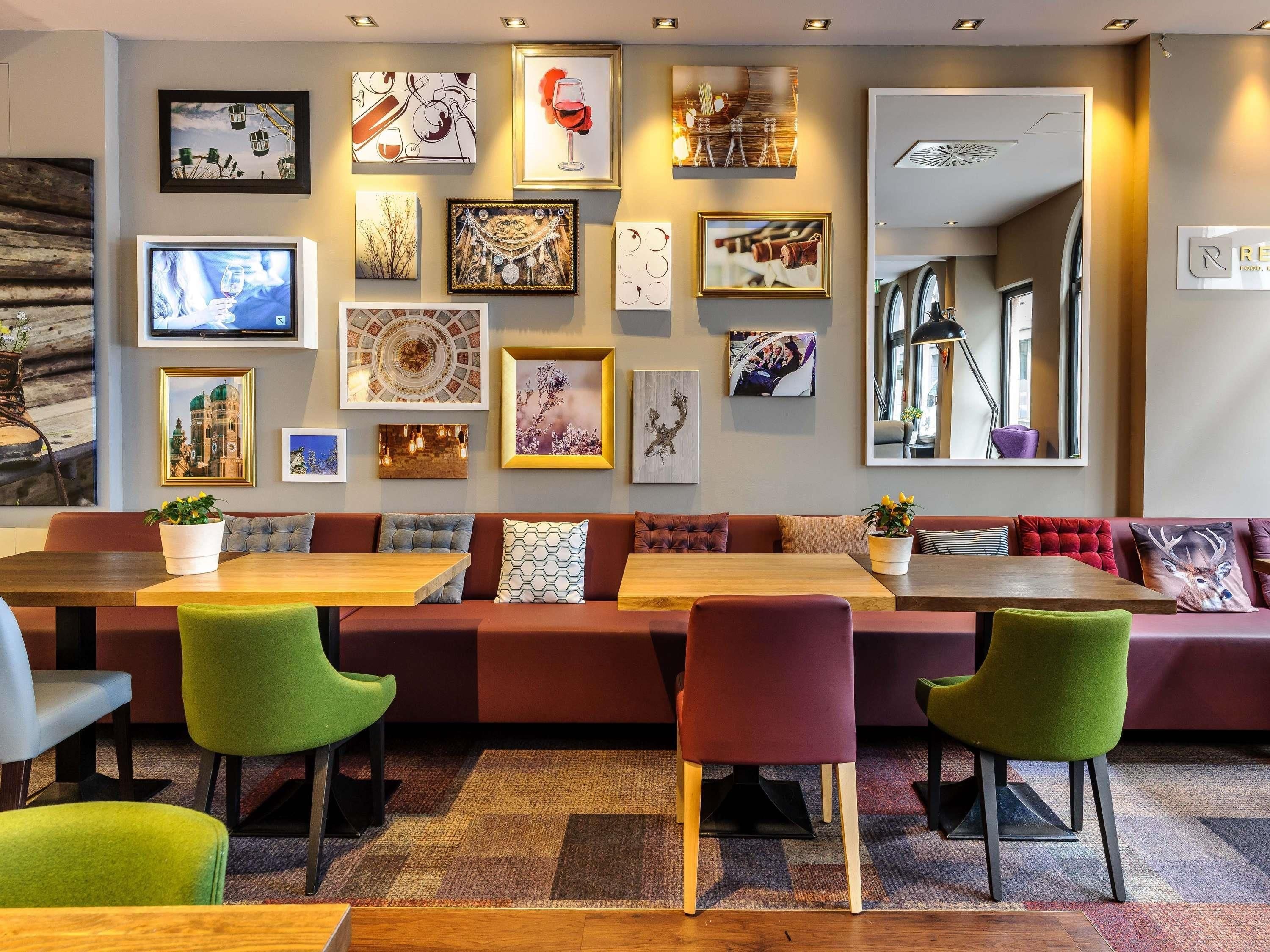 A modern lounge area with a long wooden table, cushioned seating, and a variety of framed artworks on the walls.