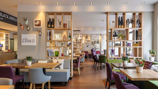 A modern interior with wooden shelves, seating areas, and a visible restaurant counter. - Mercure Muenchen City Center (Munich)