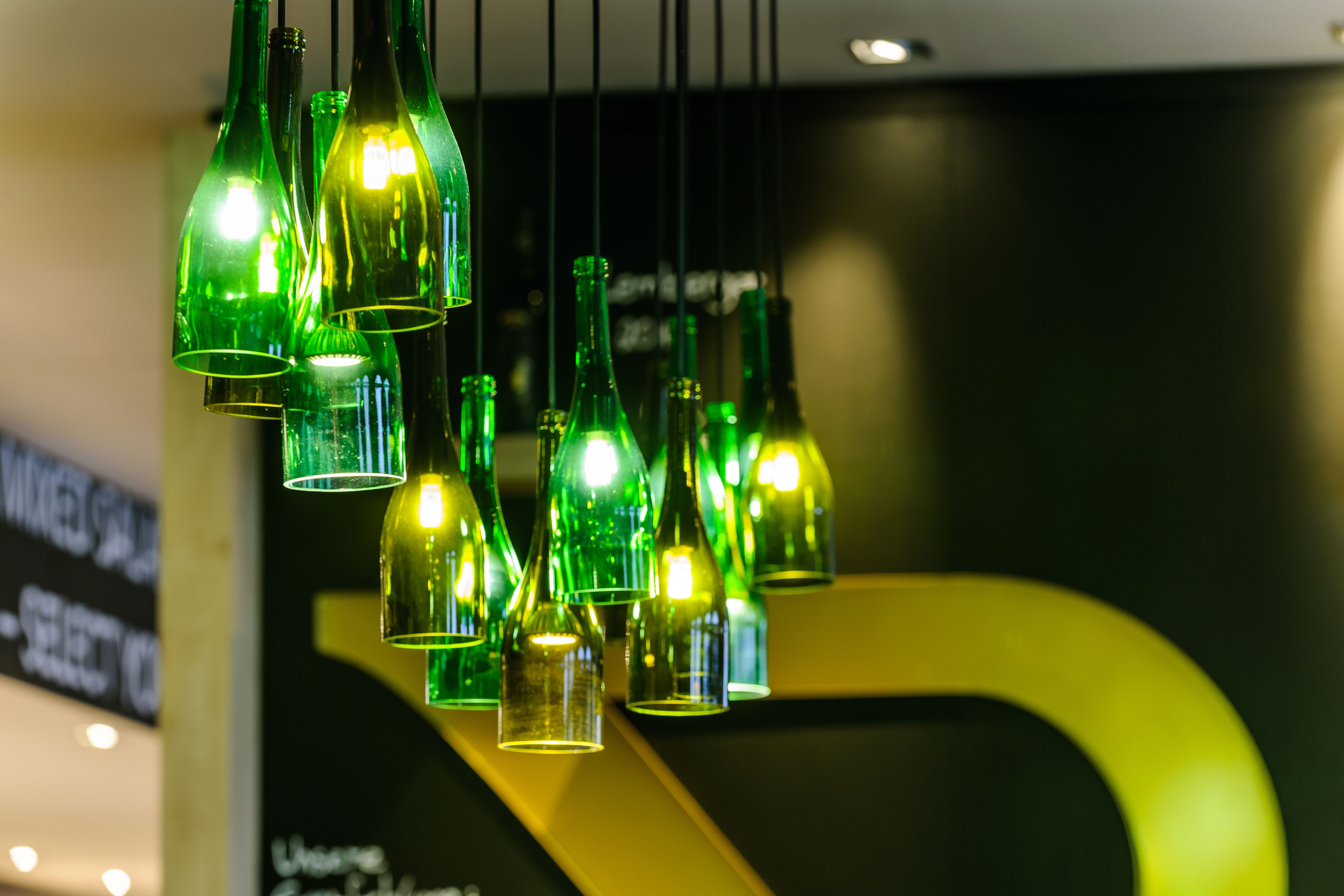 Una serie di bottiglie di vetro verde appese al soffitto, contenenti lampadine.