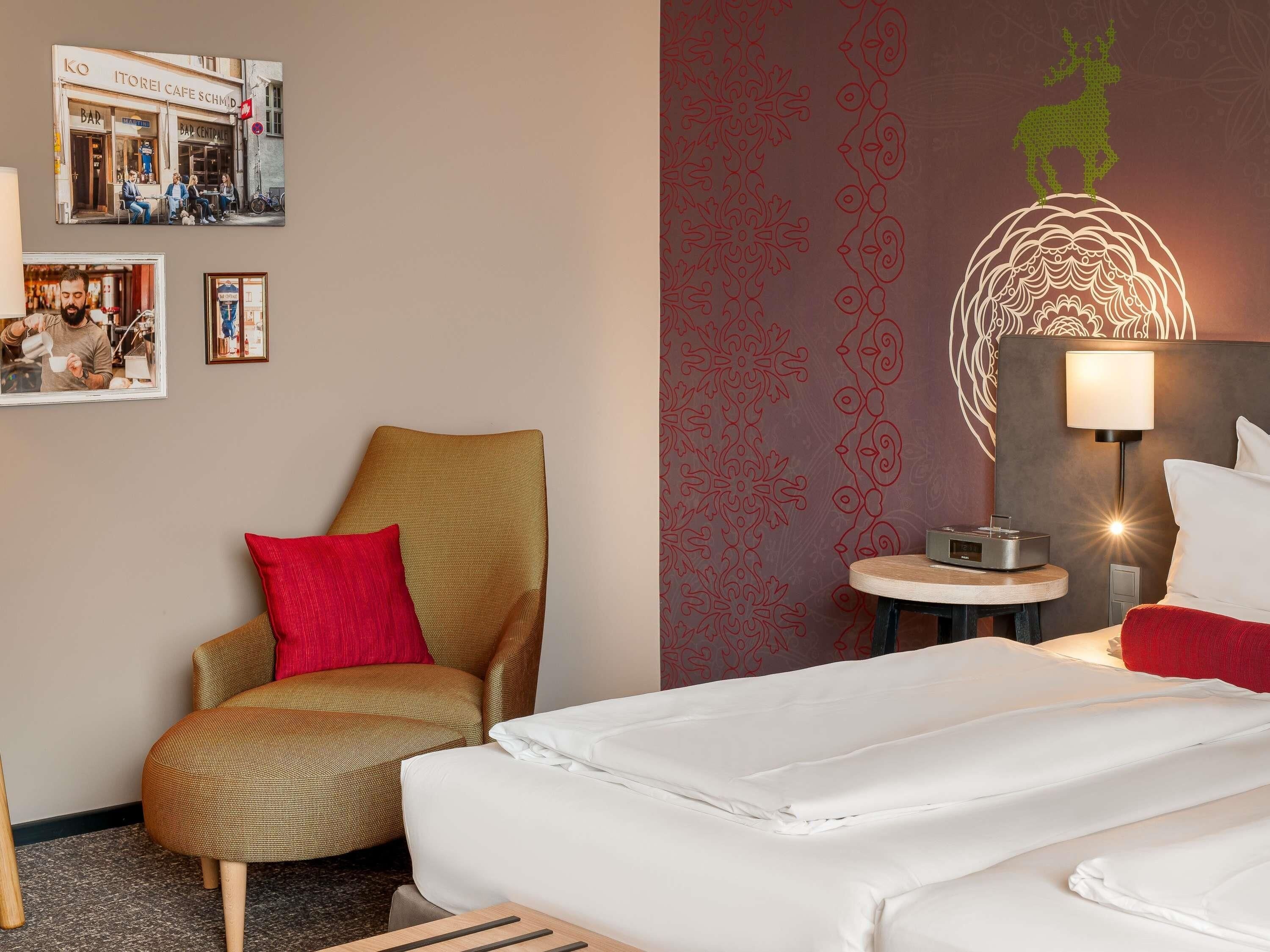 Ein Hotelzimmer mit einem Bett, einem Sessel, einem Tisch mit einer Lampe sowie Wanddekoration, darunter ein Café-Bild und ein dekoratives Wandpaneel.