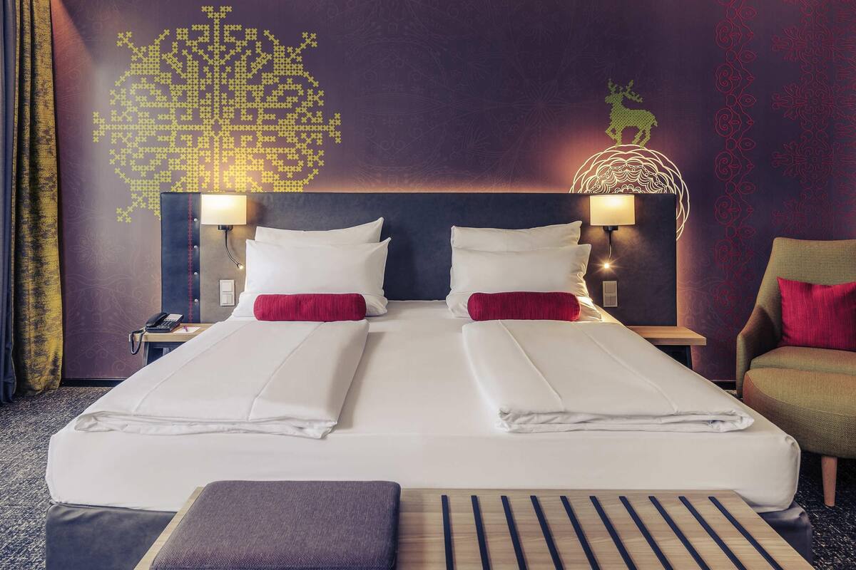 A hotel room with a large bed, two bedside tables with lamps, a chair, and a decorative wall with a geometric pattern.