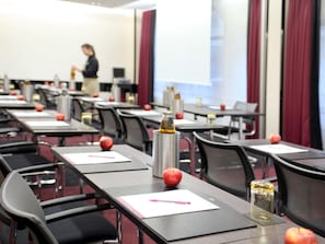 Ein Konferenzraum mit Tischen, auf jedem Tisch eine Flasche, ein Apfel und ein Notizblock.