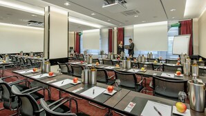 A conference room with multiple tables, chairs, and presentation equipment. - Mercure Muenchen City Center (Munich)