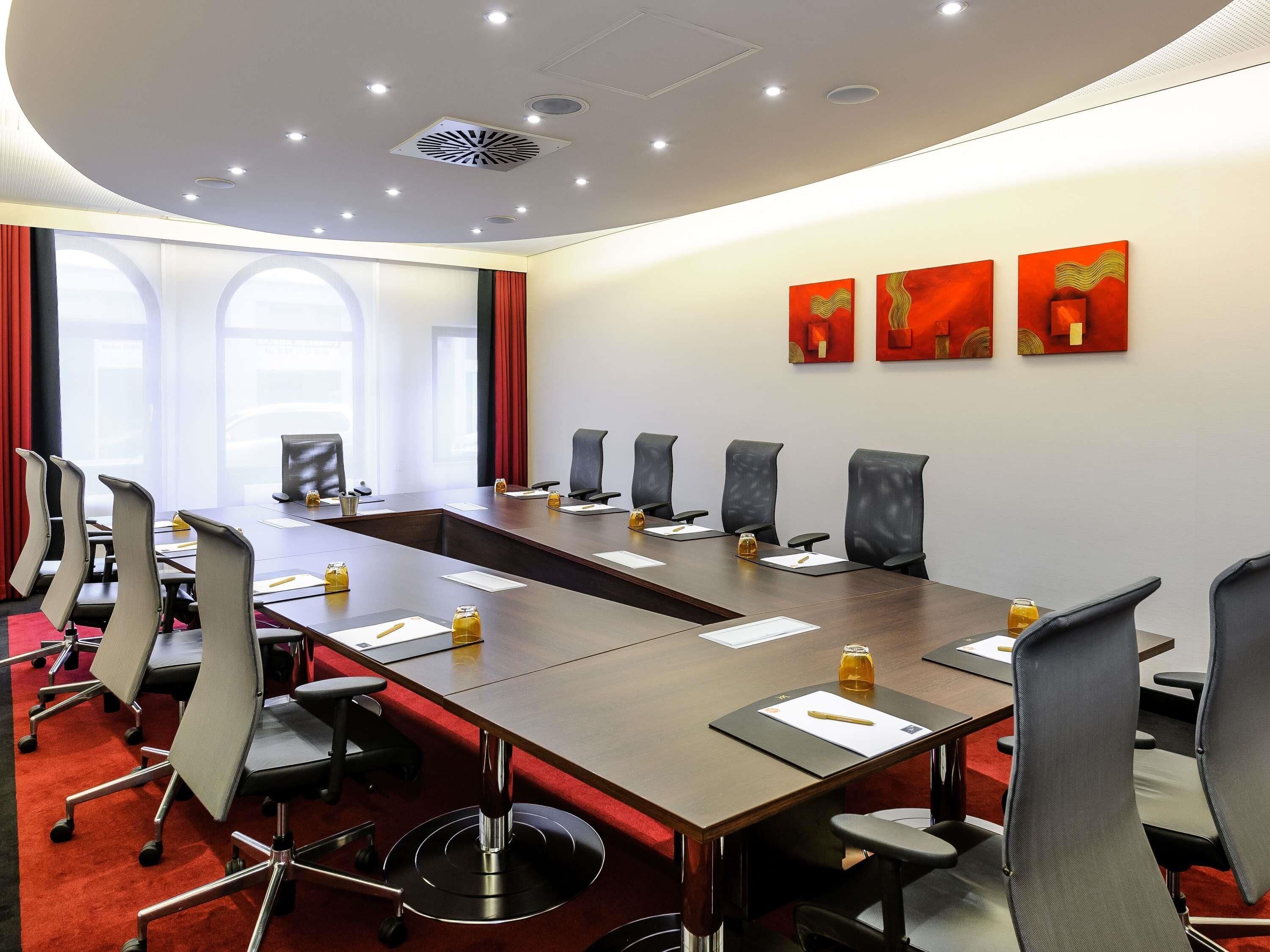 A conference room with a long table, multiple chairs, and a red carpet.
