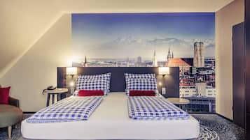 Ein Hotelzimmer mit einem Bett, das eine karierte Tagesdecke, zwei Kissen und ein rotes Akzentkissen hat. Zwei Nachttischlampen, ein Nachttisch mit Telefon und Blick auf eine Skyline mit einem markanten Turm sind ebenfalls vorhanden.