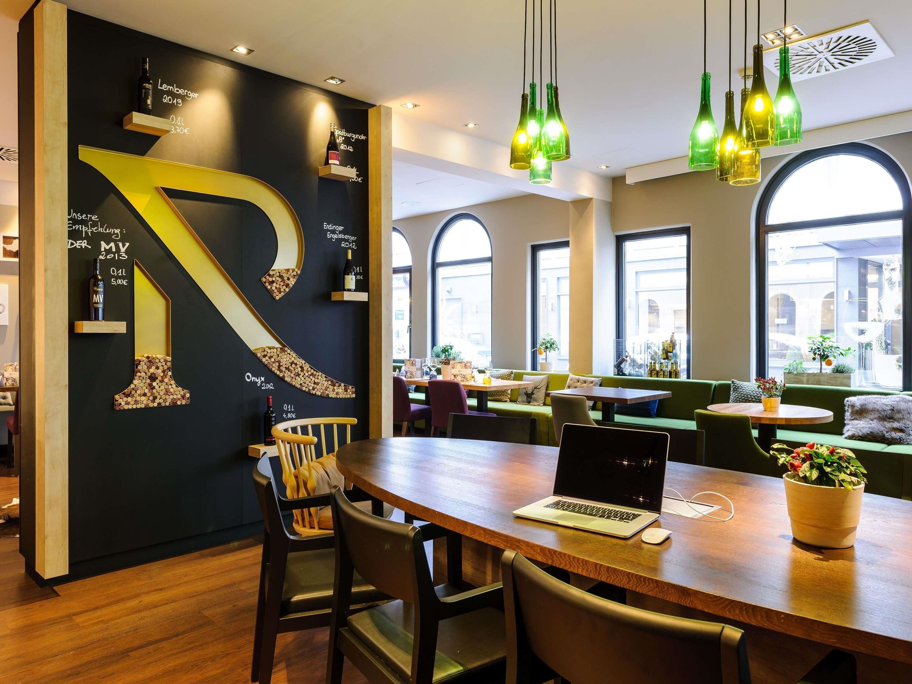 A modern restaurant interior with a large black wall featuring a prominent number '1' design, wooden tables, and green seating.
