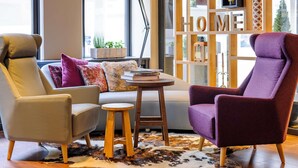 A modern living room with a sofa, two armchairs, a wooden stool, and a bookshelf. - Mercure Muenchen City Center (Munich)