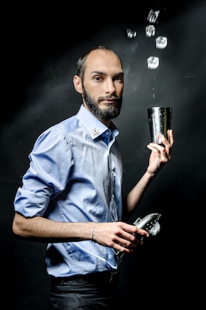 A person holding a cocktail shaker and a bottle, with ice cubes falling. - Mercure Muenchen City Center (Munich)