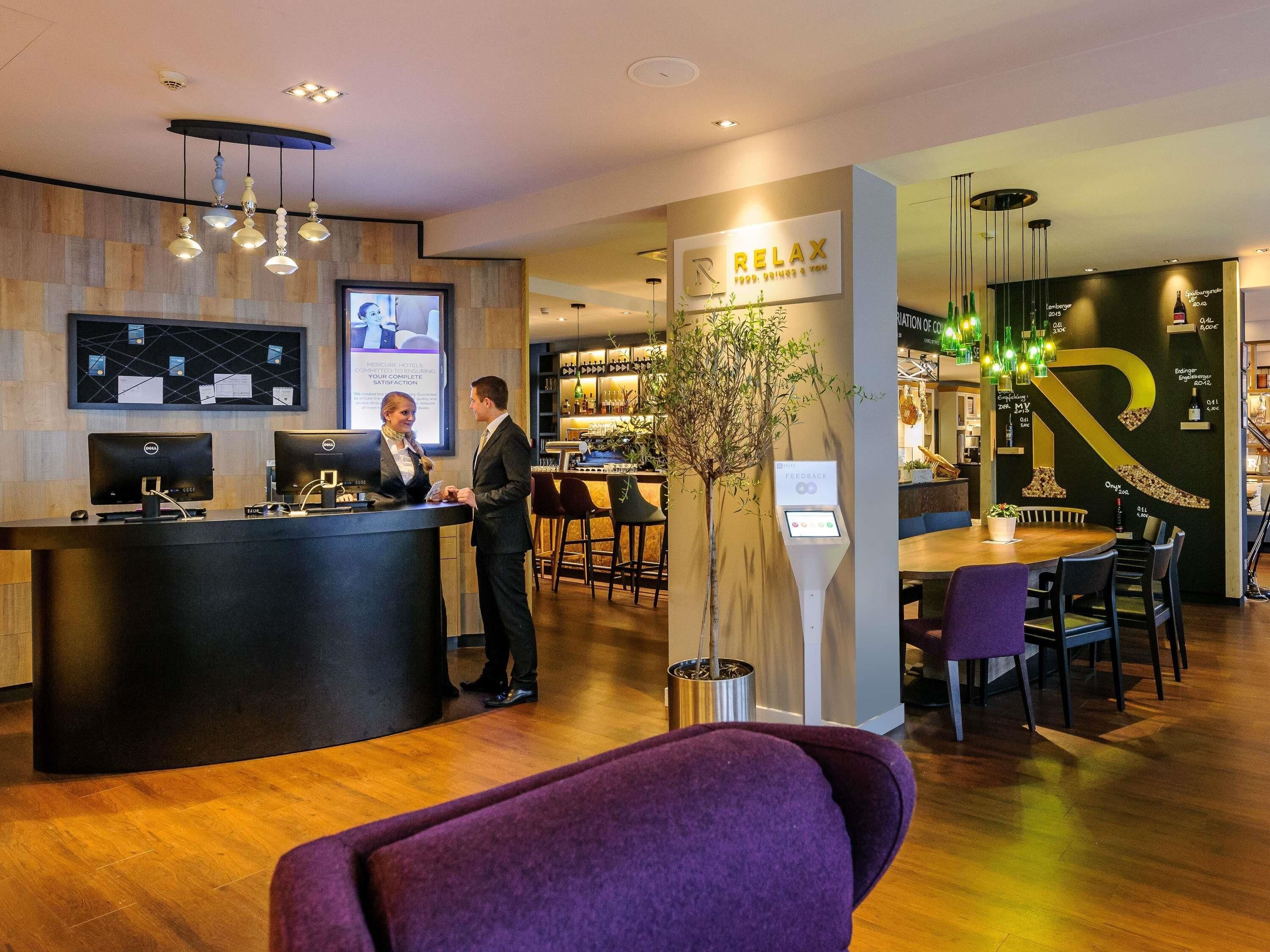 Ein Hotel-Empfangsbereich mit Empfangstresen, Computern, einer Feedback-Station und einer Bar mit Sitzgelegenheiten.
