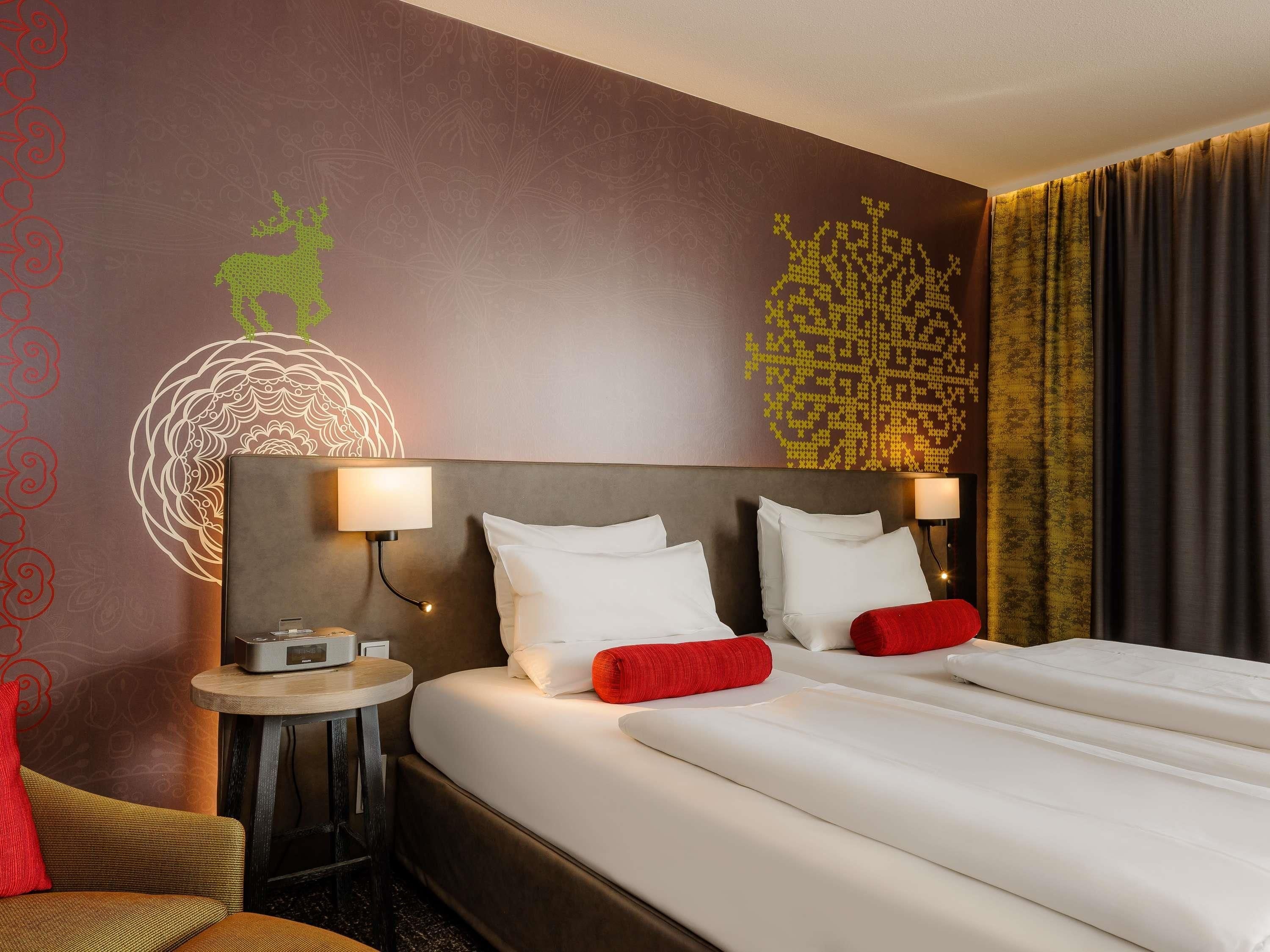 A hotel room with a large bed, two bedside tables, a wall with decorative patterns, and a curtain.