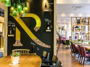 Un intérieur moderne, avec une grande lettre « R » lumineuse sur le mur, une table à manger en bois et divers types de sièges.