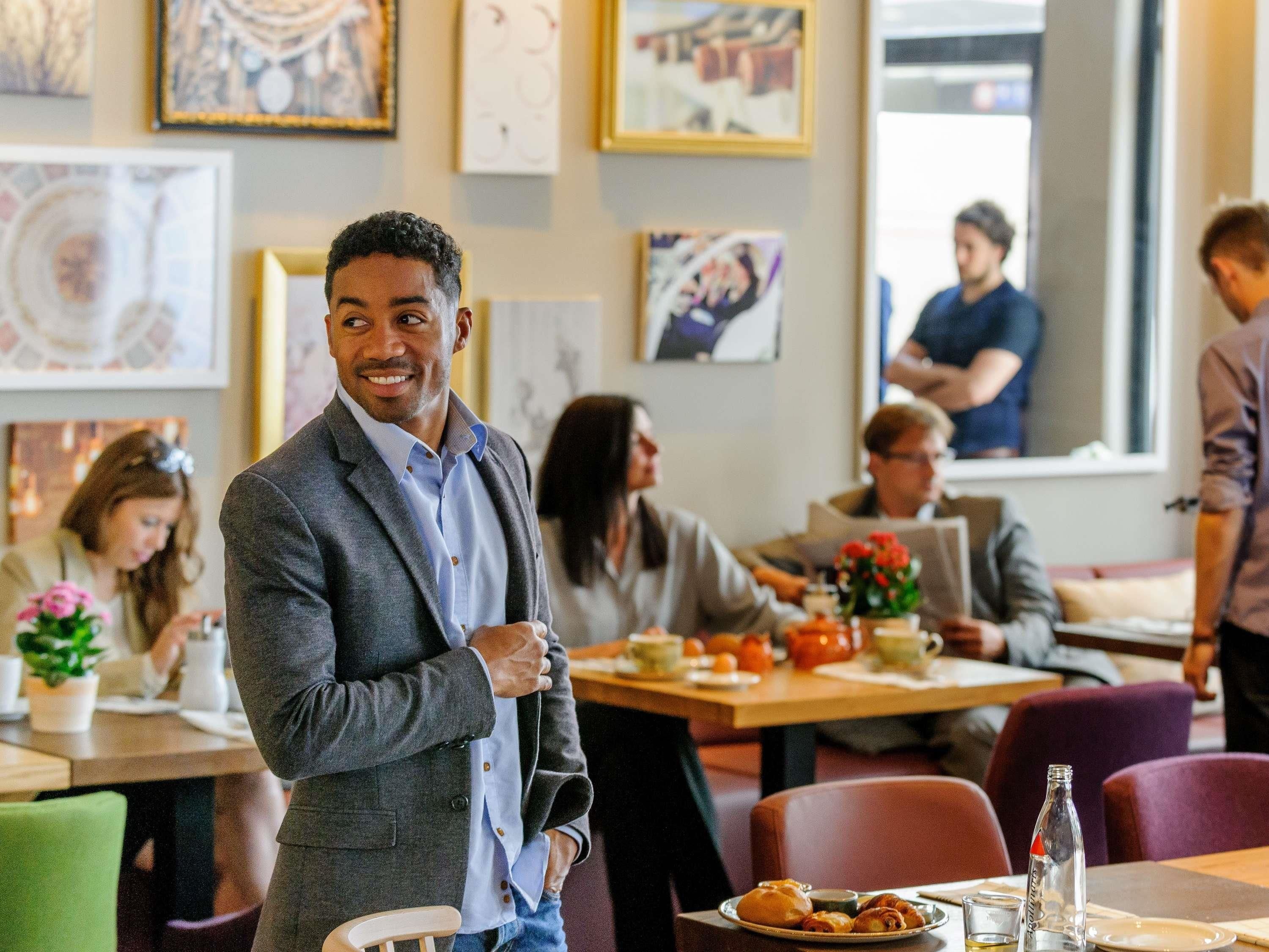A man in a suit standing in a restaurant with tables and chairs, and artwork on the walls.