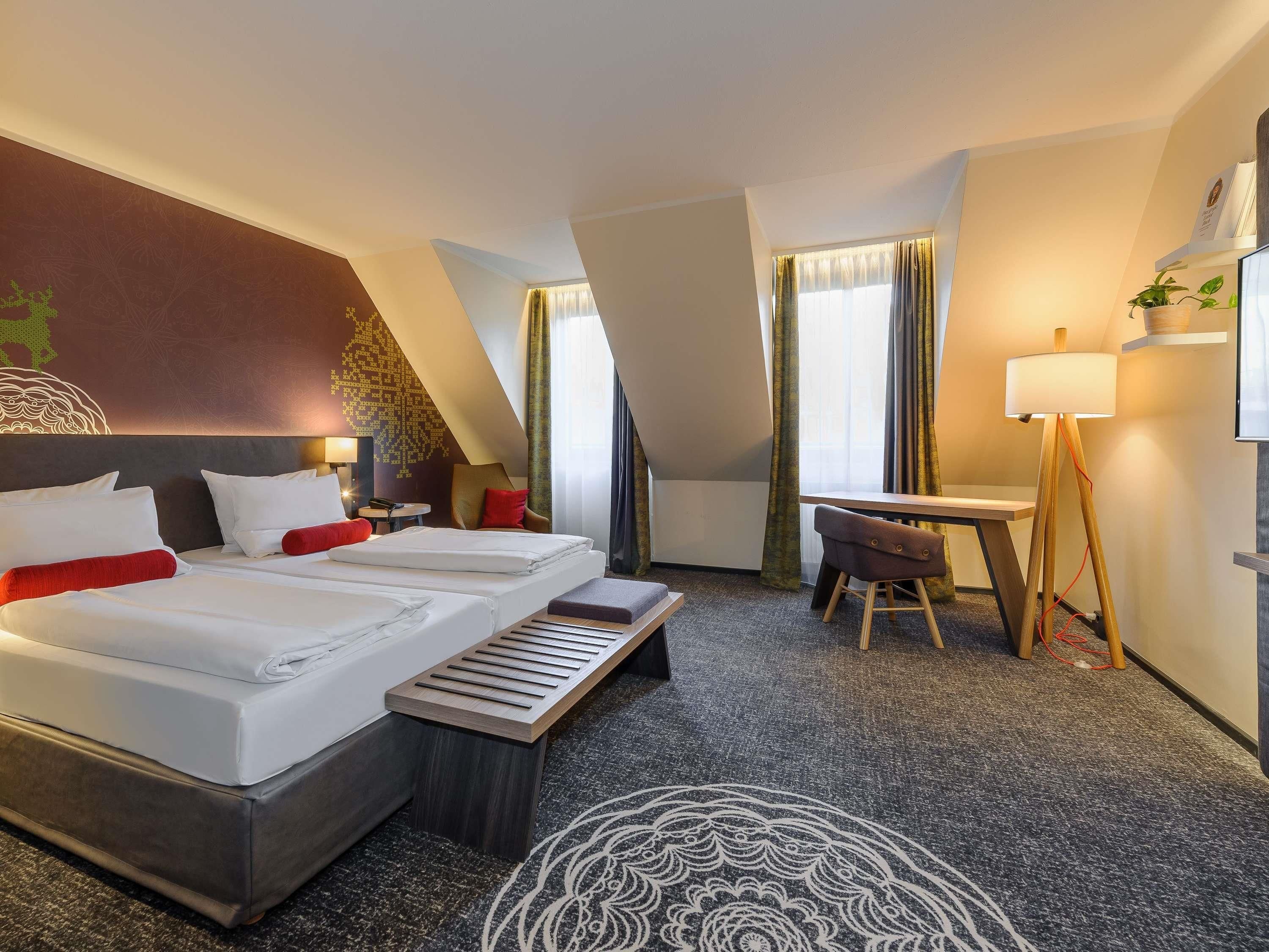 Ein Hotelzimmer mit zwei Betten, einem Schreibtisch, einem Stuhl, einer Lampe und Blick nach außen.