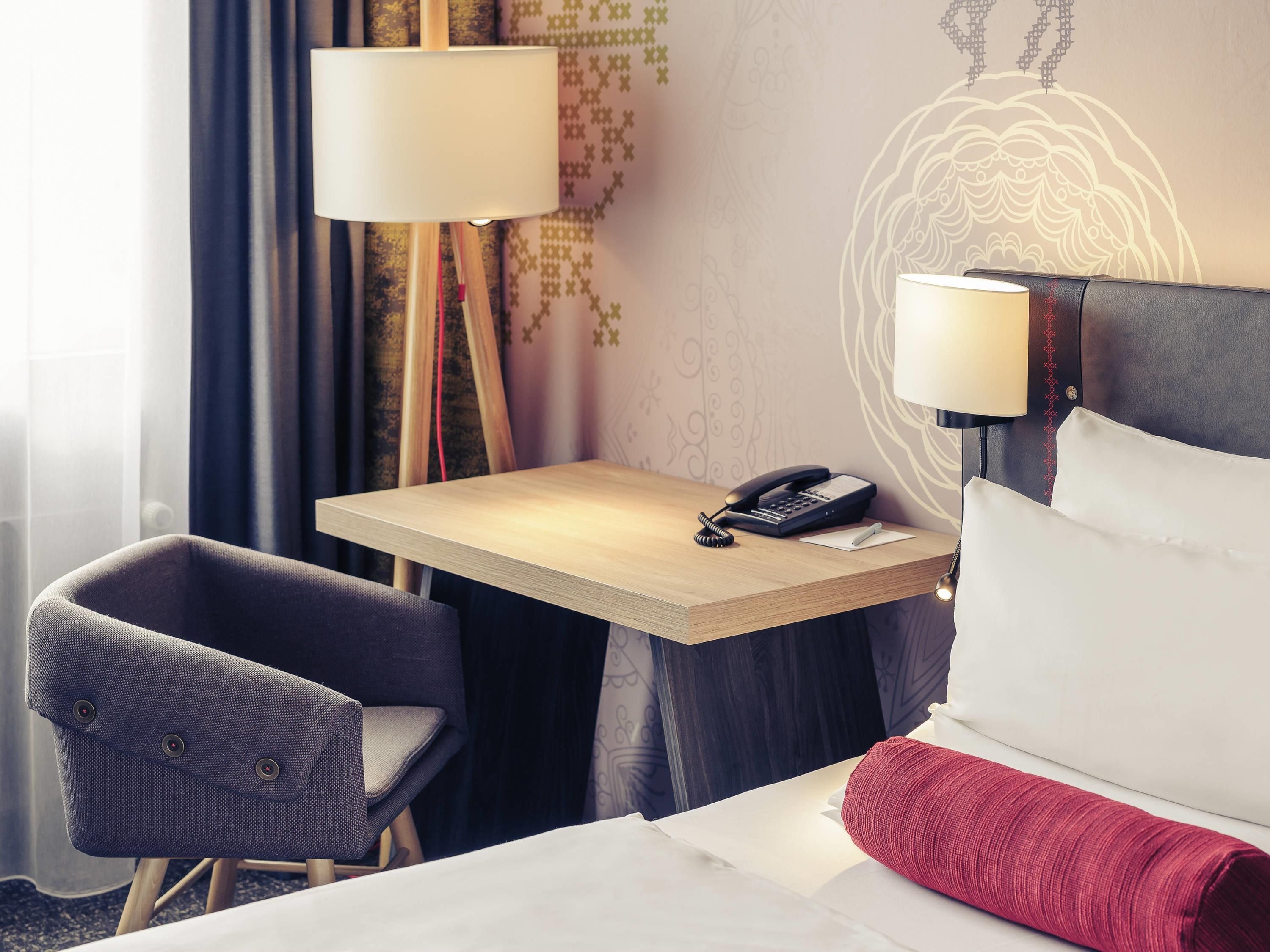 A hotel room with a bed, a desk with a telephone, a chair, and a lamp.