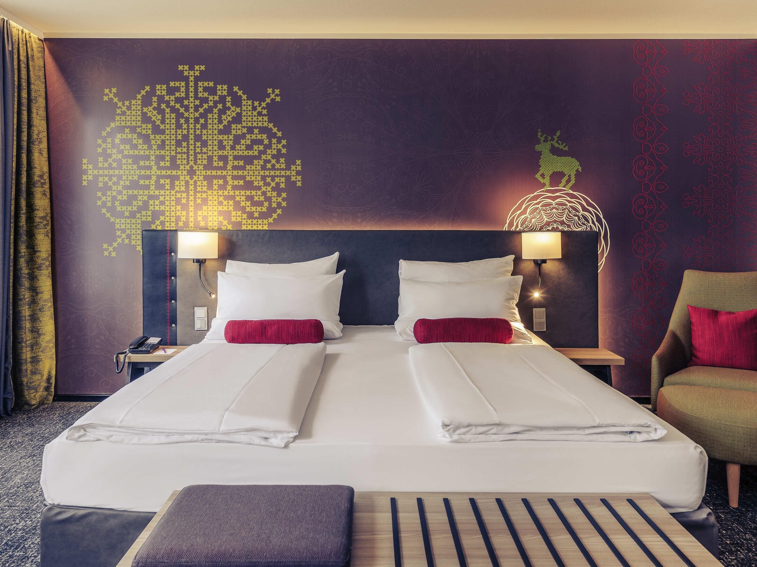 A hotel room with a large bed, two bedside tables with lamps, a chair, and a decorative wall with a geometric pattern.