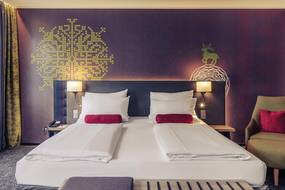 A hotel room with a large bed, two bedside tables with lamps, a chair, and a decorative wall with a geometric pattern.