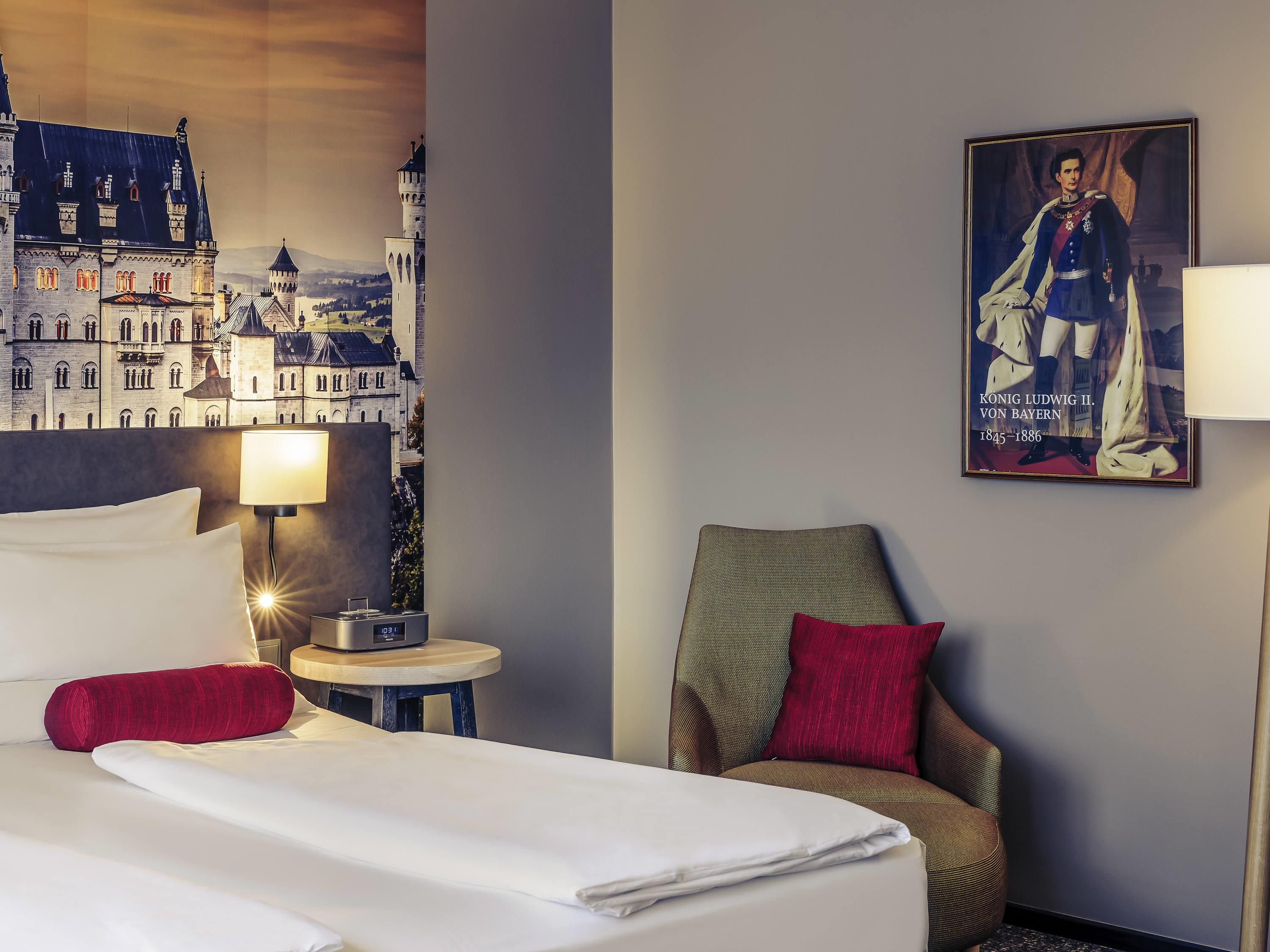 Ein Hotelzimmer mit Bett, Sessel, Lampe, Nachttisch und einem Wandbild.