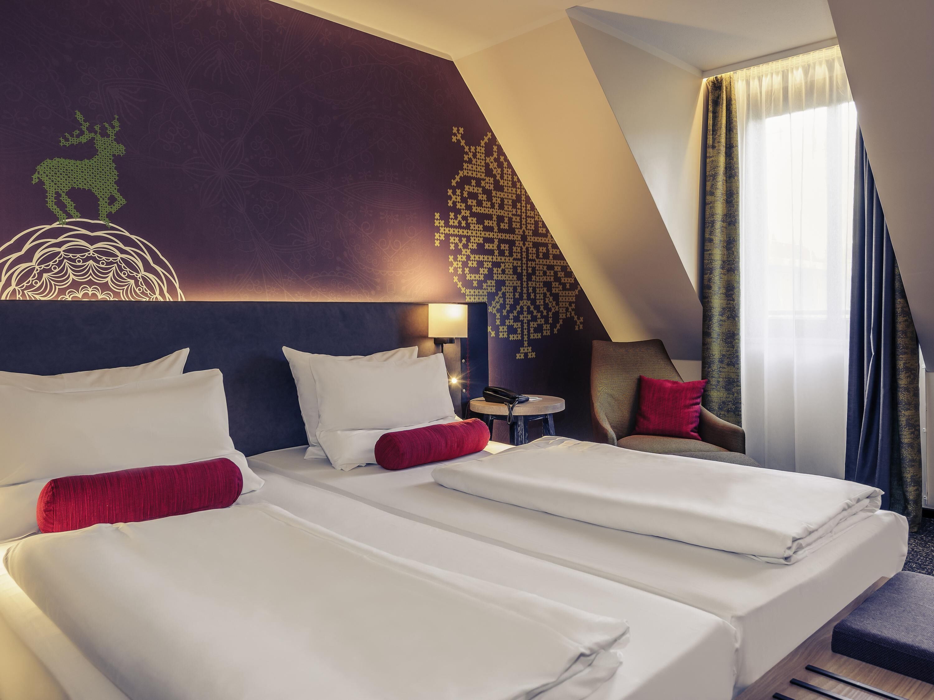A hotel room with two beds, a wall mural, a small table with a phone, and a view of the outdoors.