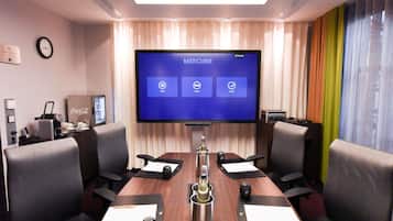 Ett konferensrum med en stor skärm som visar texten ”Mercure”, ett mötesbord med dokument och en klocka på väggen.
