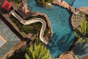 An aerial view of a swimming pool with a winding slide, surrounded by rocks and tropical plants. - The Royal Hawaiian, a Luxury Collection Resort, Waikiki (Honolulu)