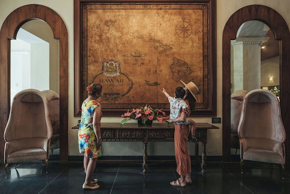 Un vestíbulo con un gran mapa de Hawái, dos sillones, una mesa con un jarrón de flores y un espejo en la pared.