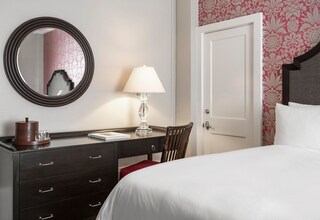A hotel room with a bed, a dresser with drawers, a lamp, a mirror, and a door.