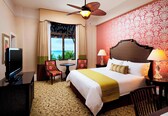A hotel room with a bed, a television, a desk, a chair, and a view of the ocean.